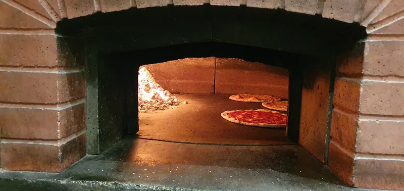 Pizzas cooking over an open flame in the wood-fired oven